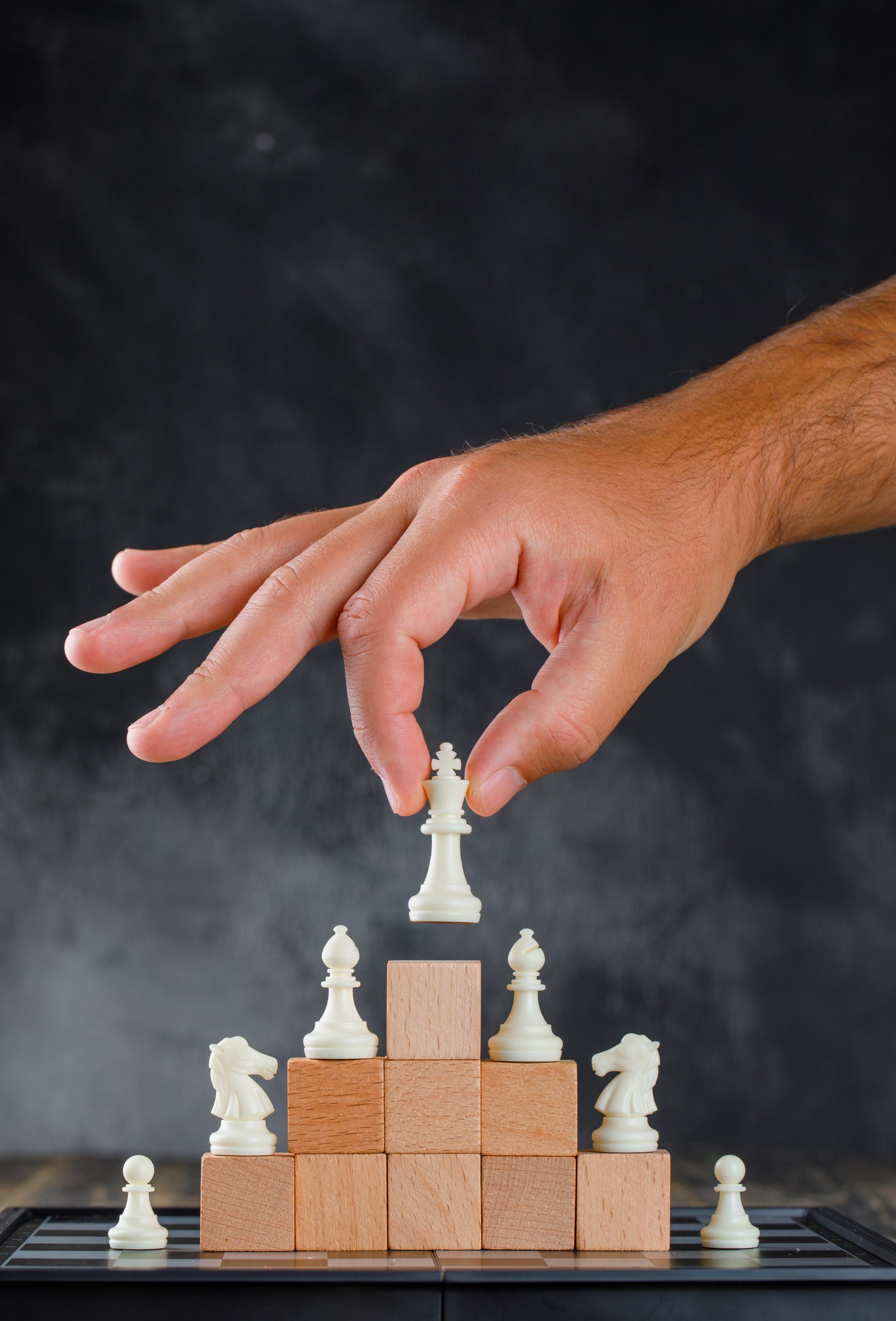 Business success concept with chessboard on wooden and foggy background side view. man placing figure on pyramid of blocks.